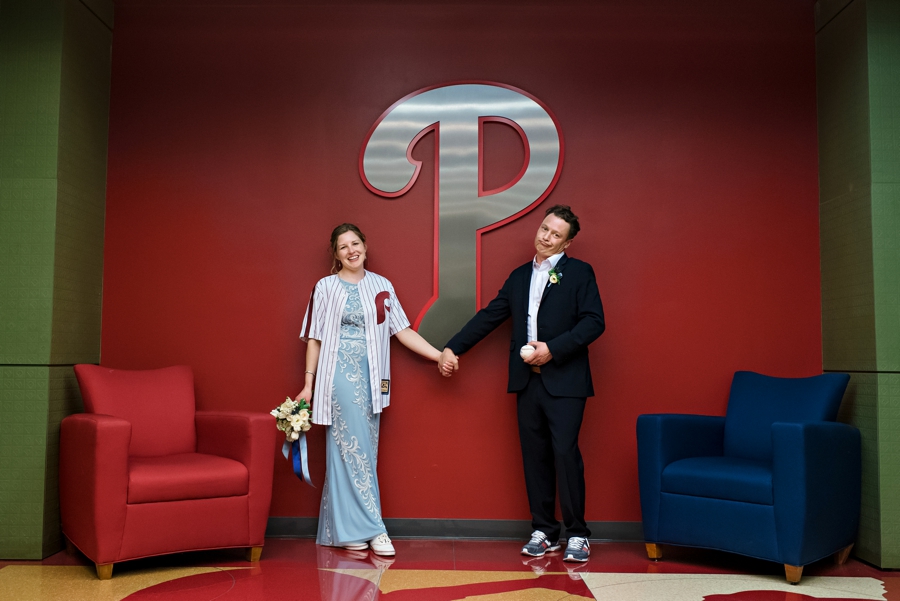 A bride and groom hold hands under the Phillies sign outside of the game suites.